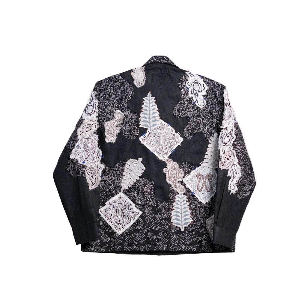 A black long-sleeve jacket with an intricate patchwork design of white, gray, and light blue lace and embroidered motifs, shown flat against a light beige background.
