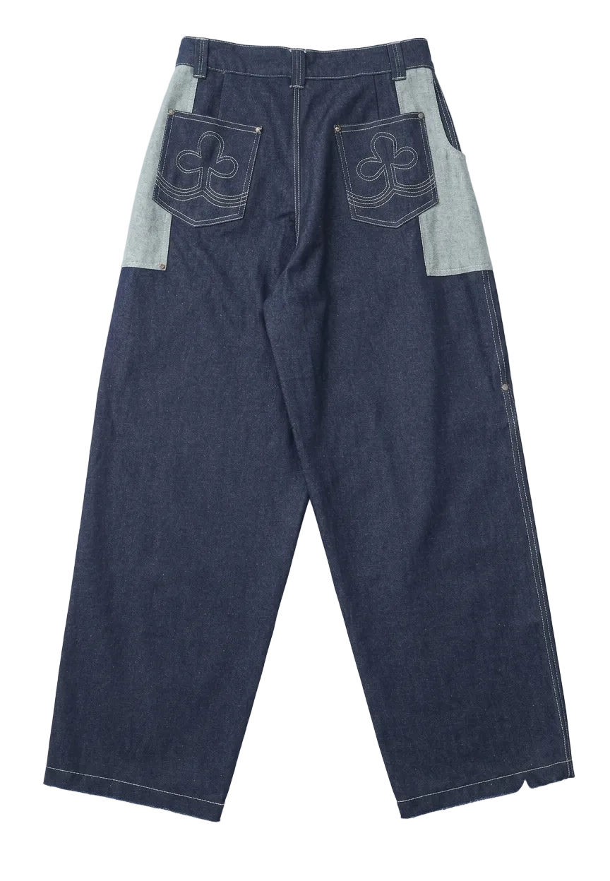 A pair of dark indigo denim pants with light gray contrast panels on the upper thighs and back pocket flaps featuring white embroidered logos, laid flat against a white background.