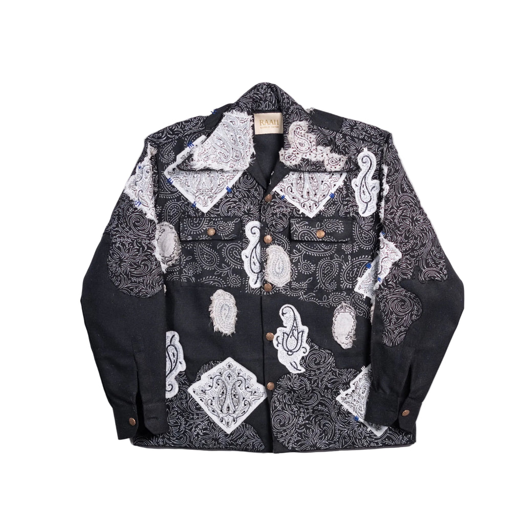 A black button-up shirt jacket featuring a patchwork design with white and gray paisley and bandana prints, displayed flat against a light beige background.