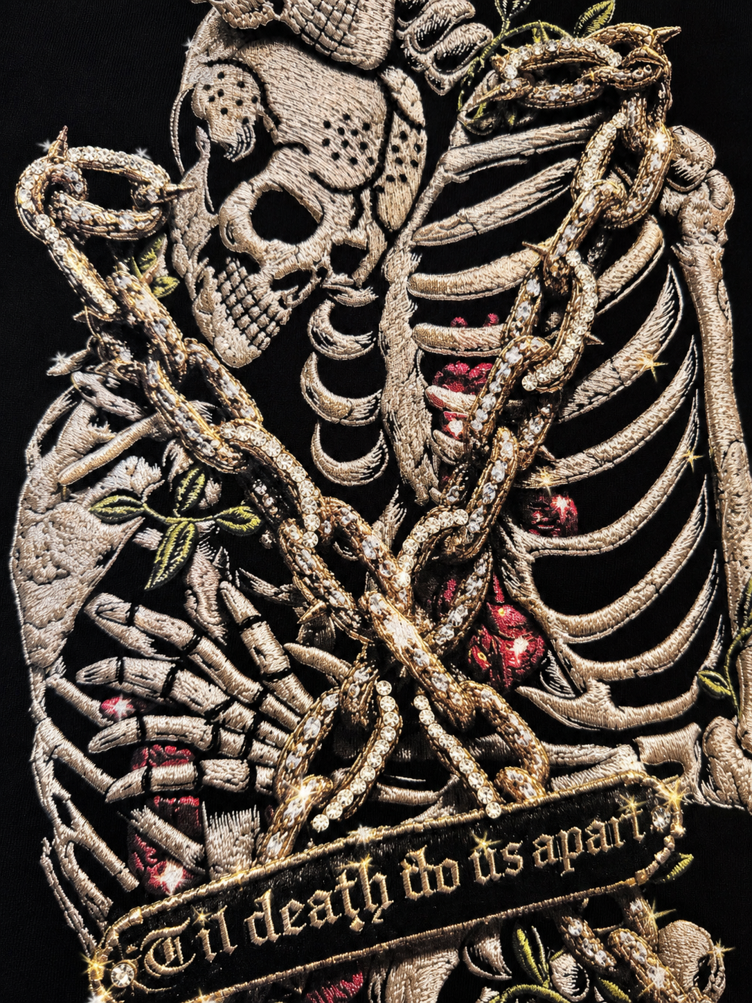 Close-up of a gothic embroidered patch featuring a skeleton with crossed bones, thorny chains, red roses, and a banner reading 'til death do us apart' on a black background.