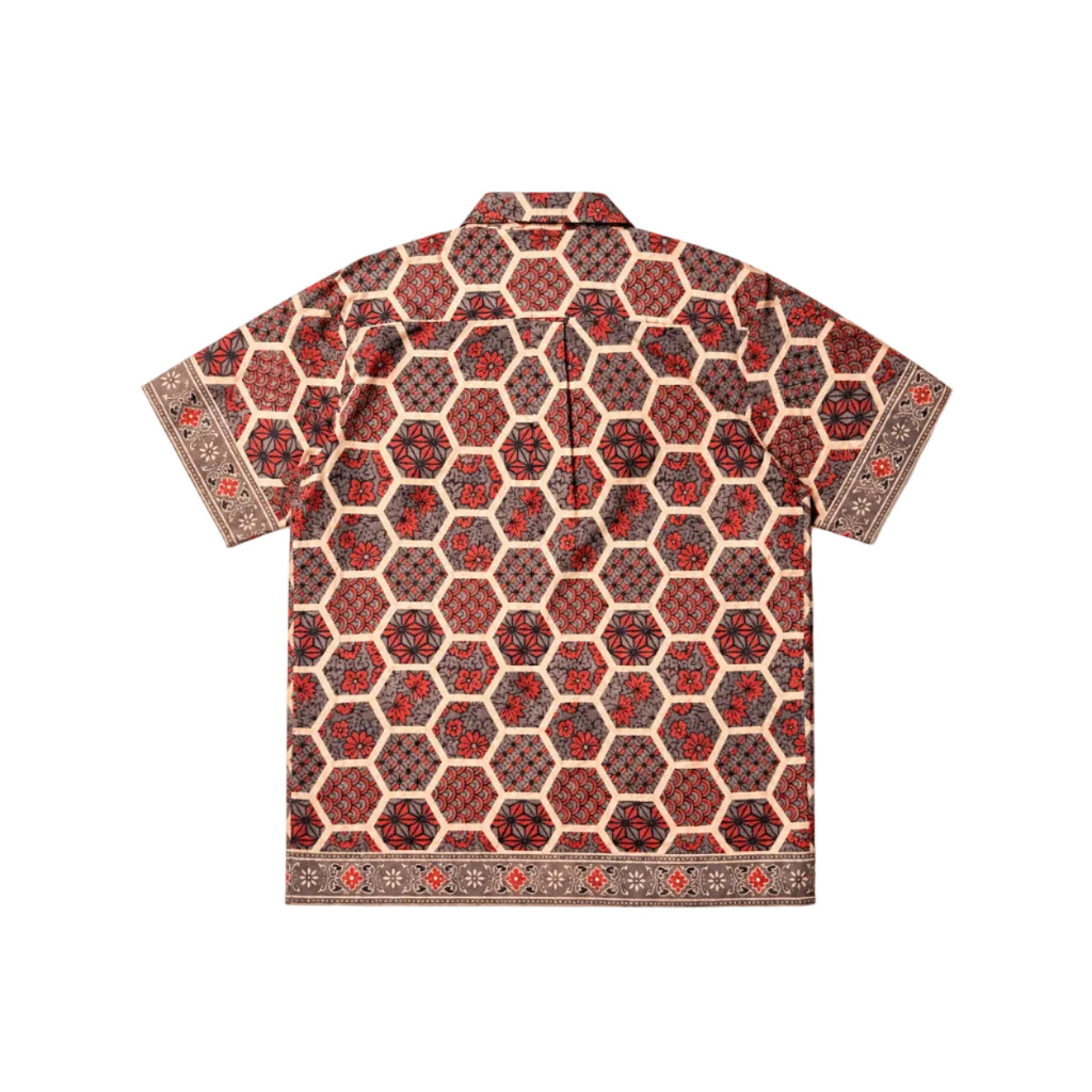 A short-sleeve button-up shirt with a detailed geometric and floral pattern in red, black, and beige, displayed flat against a light gray background.