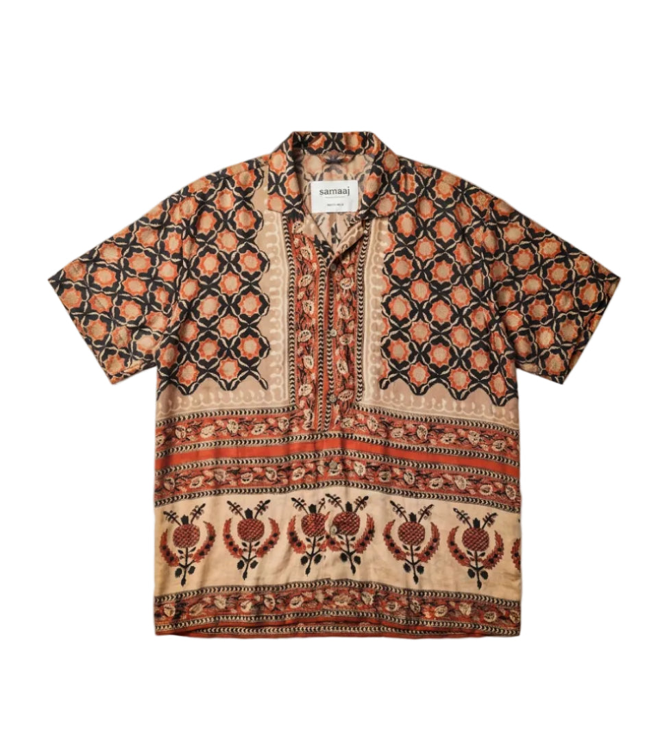 A short-sleeve button-up shirt with a complex geometric and floral block print in brown, rust orange, and beige, laid flat against a light gray background.