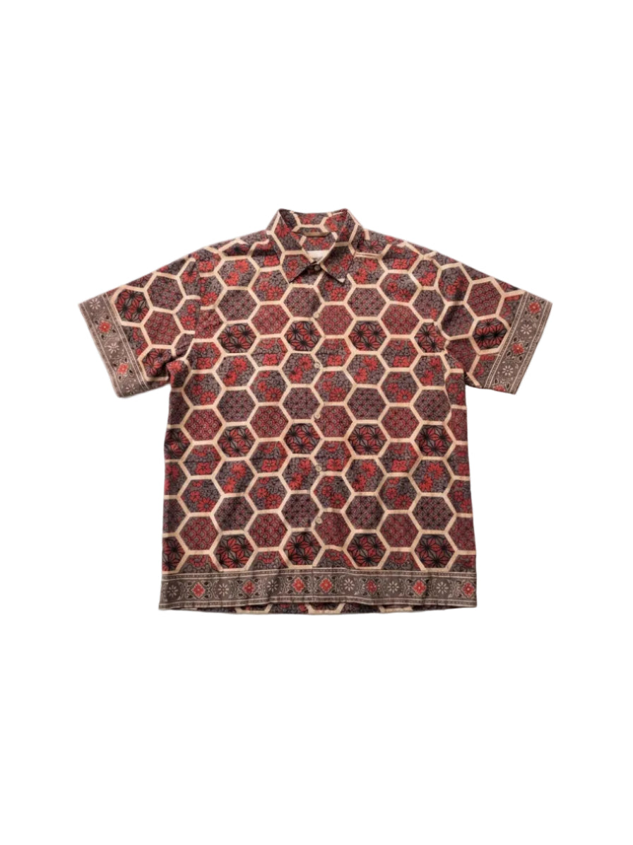 A short-sleeve button-up shirt with an all-over geometric hexagon pattern in dark red, brown, and beige, laid flat against a light gray background.