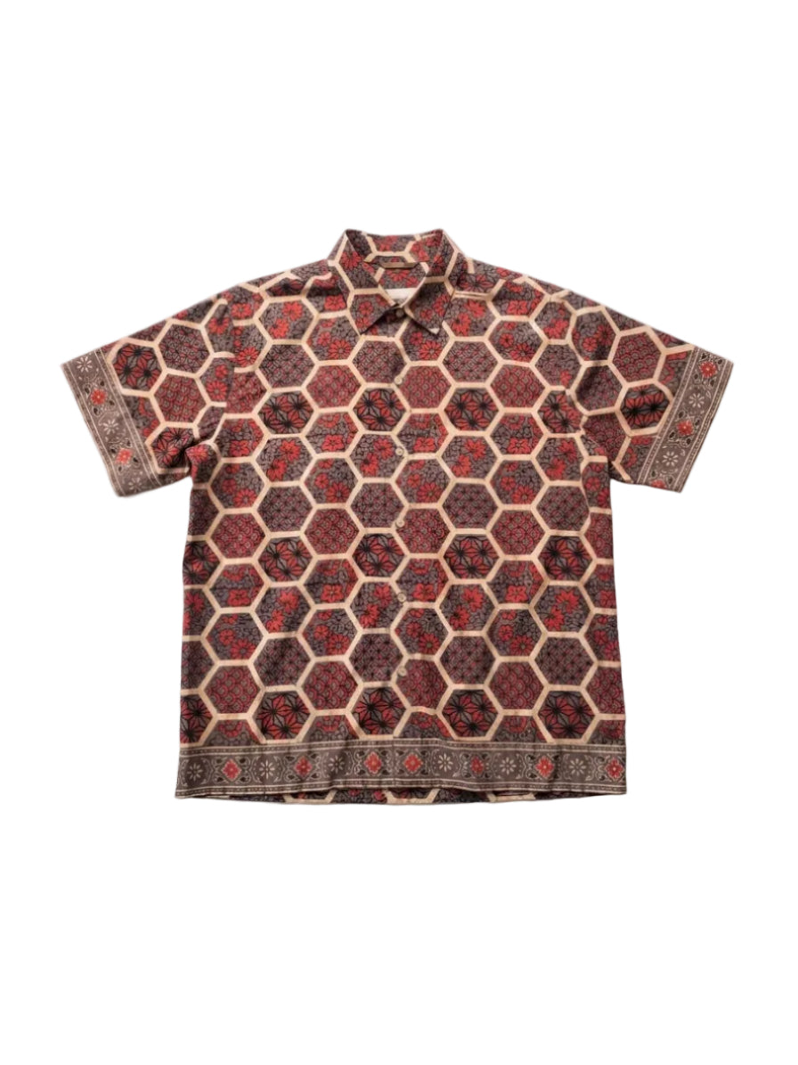 A short-sleeve button-up shirt with an all-over geometric hexagon pattern in dark red, brown, and beige, laid flat against a light gray background.