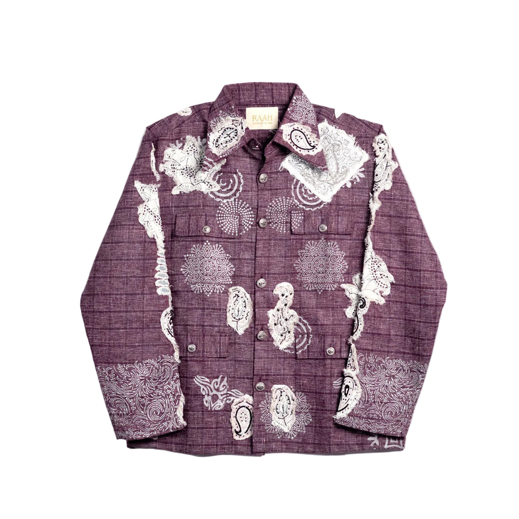 A long-sleeve button-up shirt in a deep plum purple color, featuring a subtle plaid texture and white printed illustrations of skulls, flowers, and paisley patterns, laid flat against a light off-white background.